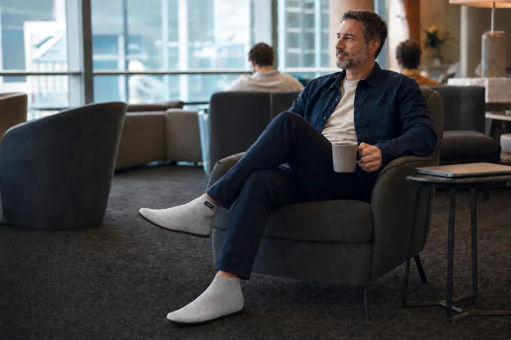 Traveler seated in an airport lounge wearing ash gray COOPS High Tops.