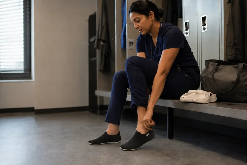 Nurse changing into black COOPS Low Tops in a locker room.