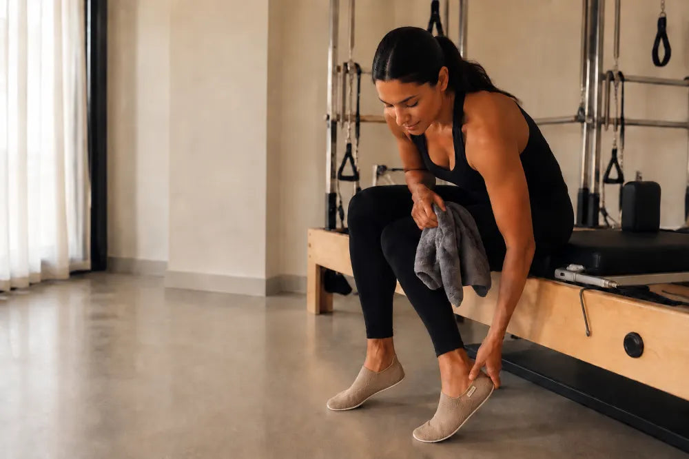 Woman stepping into sand COOPS Low Tops beside a reformer.