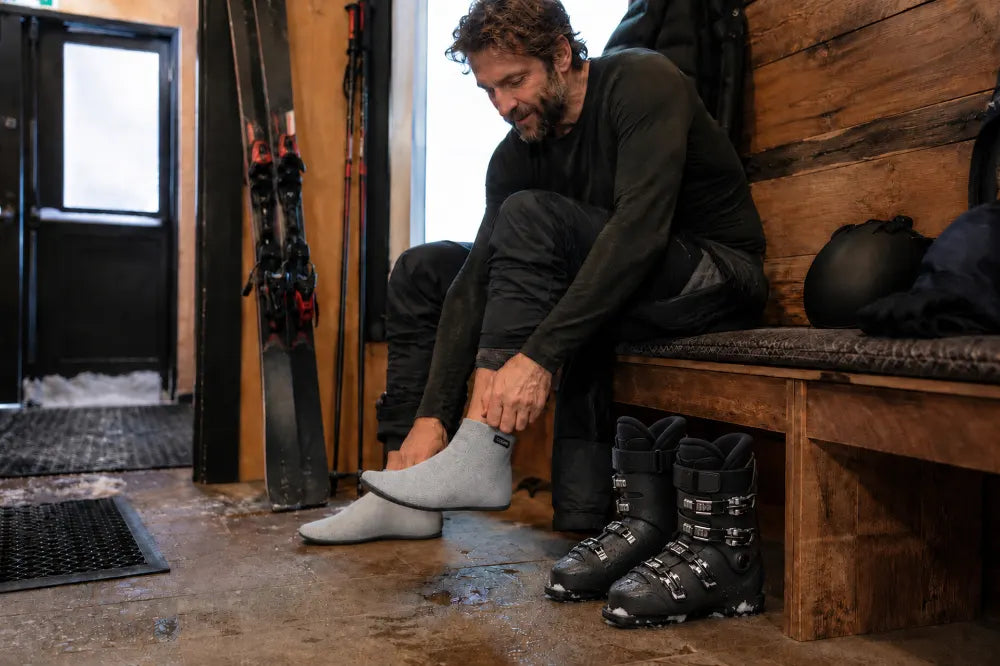 Skieur retirant ses chaussures de ski à côté de COOPS High Tops gris cendré.