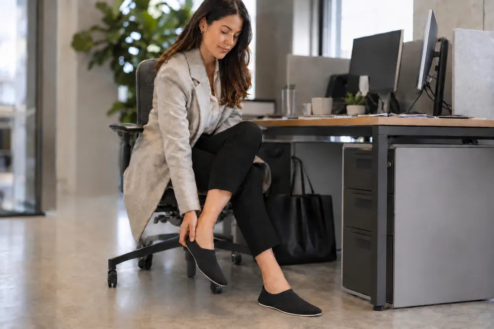 Commuter at her desk slipping on black COOPS Low Tops.