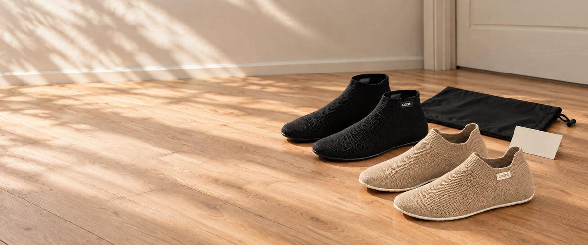 Black COOPS High Tops and Sand COOPS Low Tops on a wooden floor beside the COOPS wash bag
