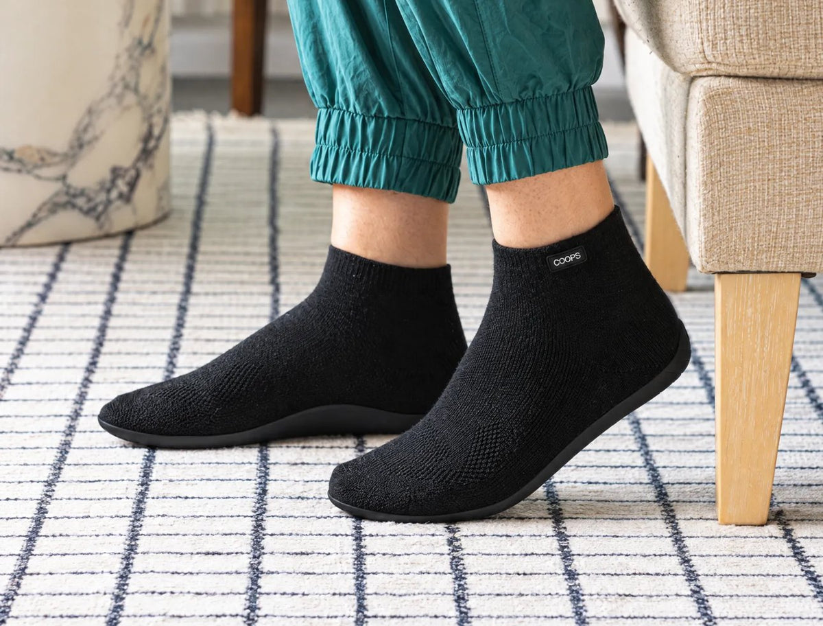 Woman sitting on a bench in a sunlit bedroom wearing Sand COOPS low top sock shoes