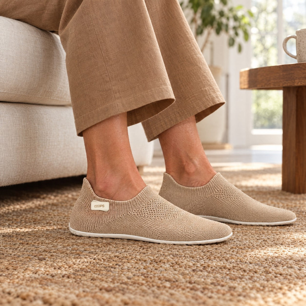 A person relaxing on a sofa wearing Sand COOPS sock shoes on a woven rug at home