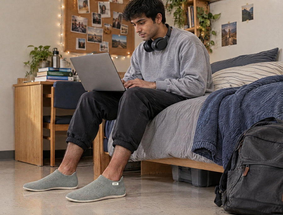 Student standing in his dorm room with a laptop, wearing Black COOPS Low Top sock shoes