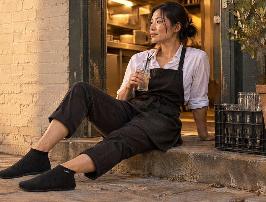Waiter resting on a bench outside a restaurant after a shift, wearing Black COOPS High Top sock shoes