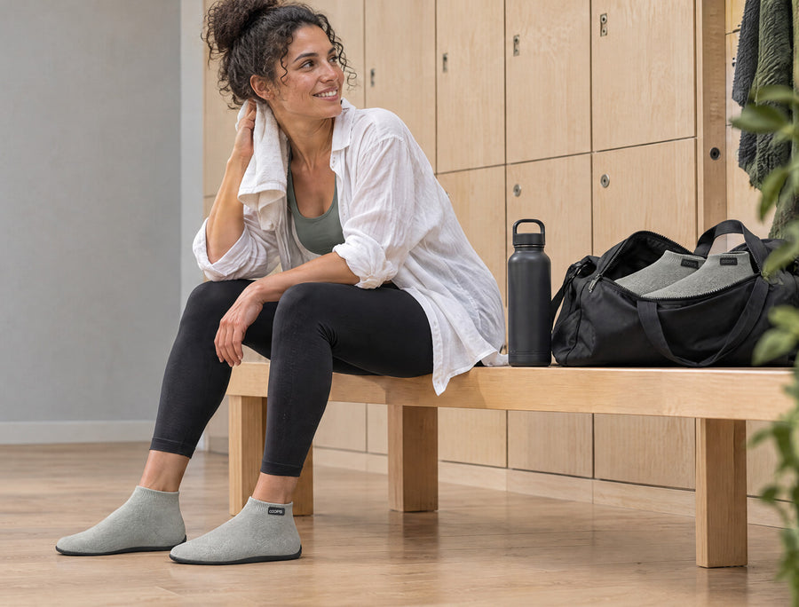 Mujer en un banco del gimnasio después de entrenar, con zapatos calcetín COOPS Low Top negros