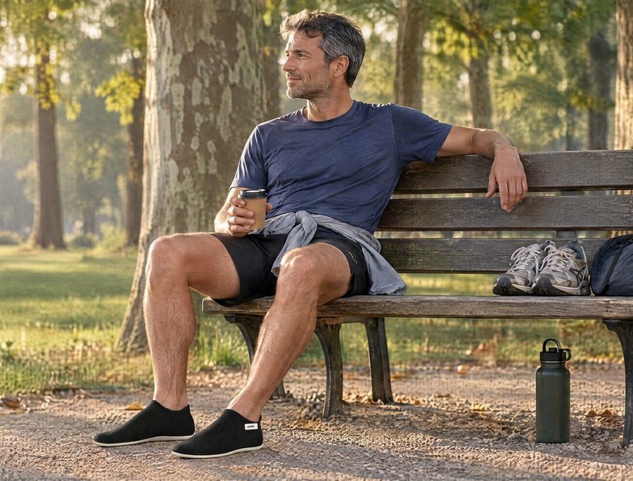 Runner drinking water on a park bench by his car, running shoes beside him, wearing Black COOPS Low Top sock shoes