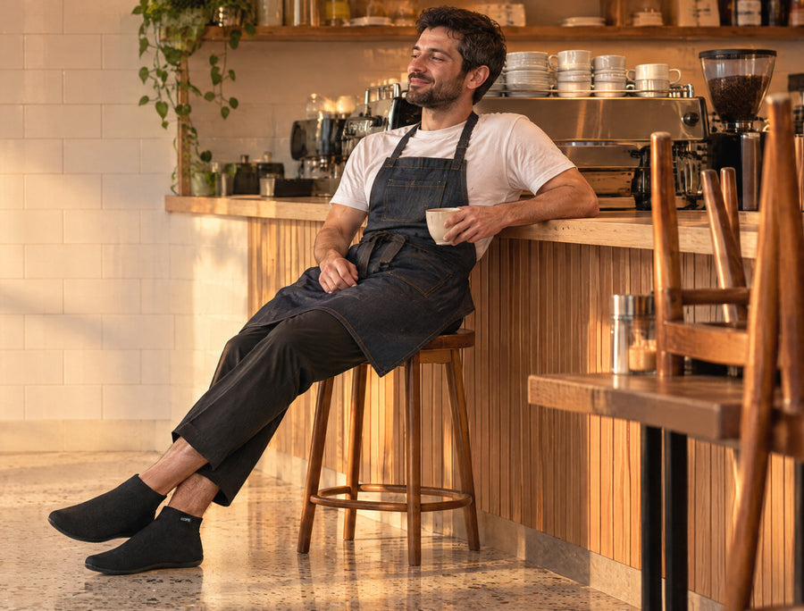 Worker resting on a bench after a shift, work boots off beside him, wearing Ash Gray COOPS High Top sock shoes
