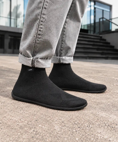 Black COOPS High Top sock shoes with cuffed grey jeans on a city plaza