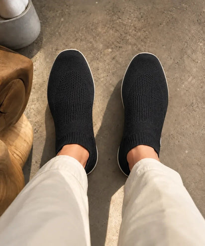 Looking down at Black COOPS Low Top sock shoes and cream trousers