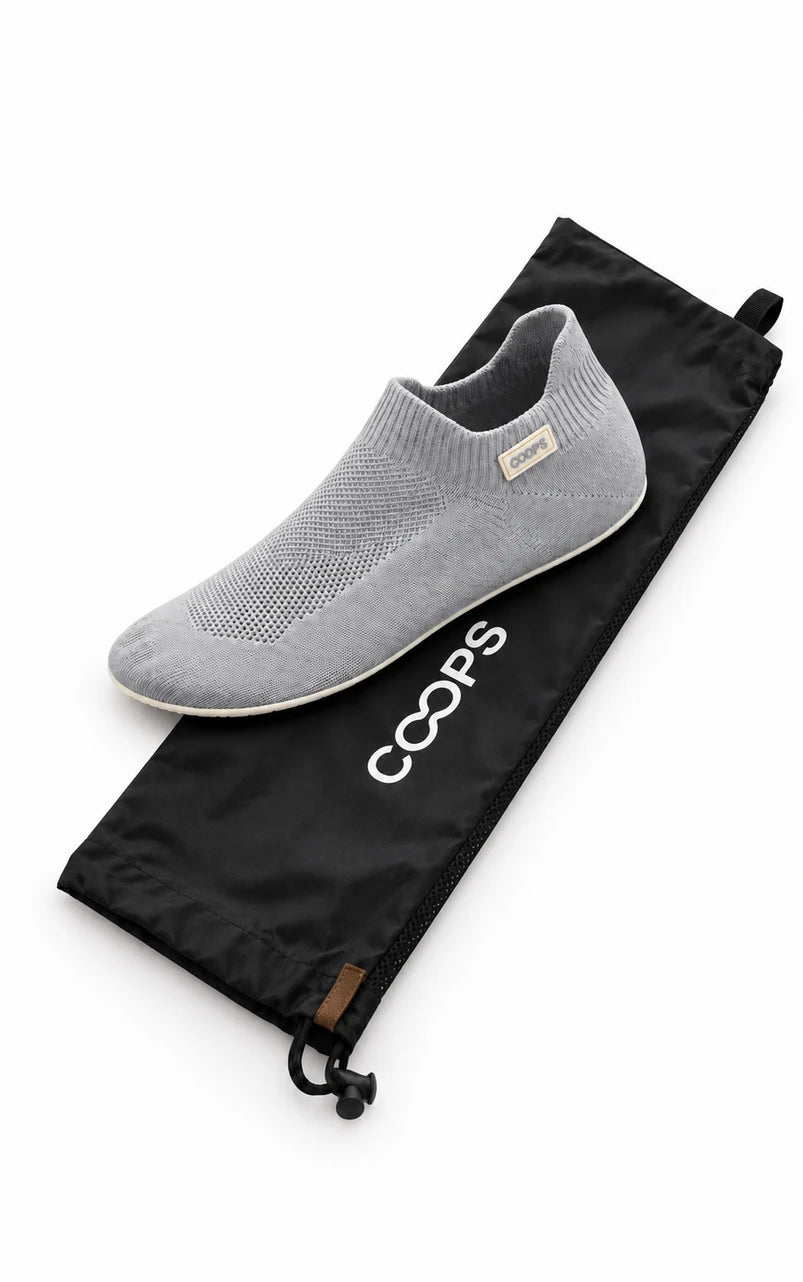 An Ash Gray COOPS Low Top sock shoe resting on the black COOPS wash bag
