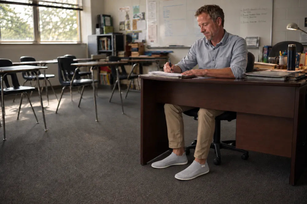Teacher grading papers at his desk in ash gray COOPS Low Tops.