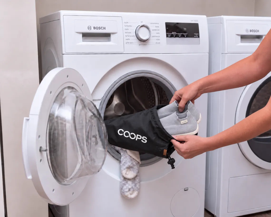 Lightly soiled Ash Gray COOPS low top sock shoes on a COOPS wash bag, being loaded into a washing machine