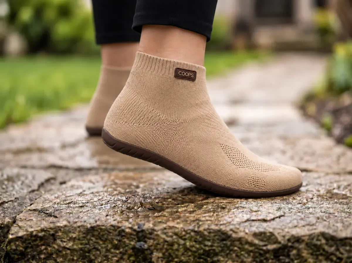 Sand COOPS high top sock shoes on a stone path, showing the rubber outsole